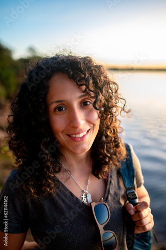 Mixed-race woman looking at camera and smiling while enjoying outdoors at sunset.