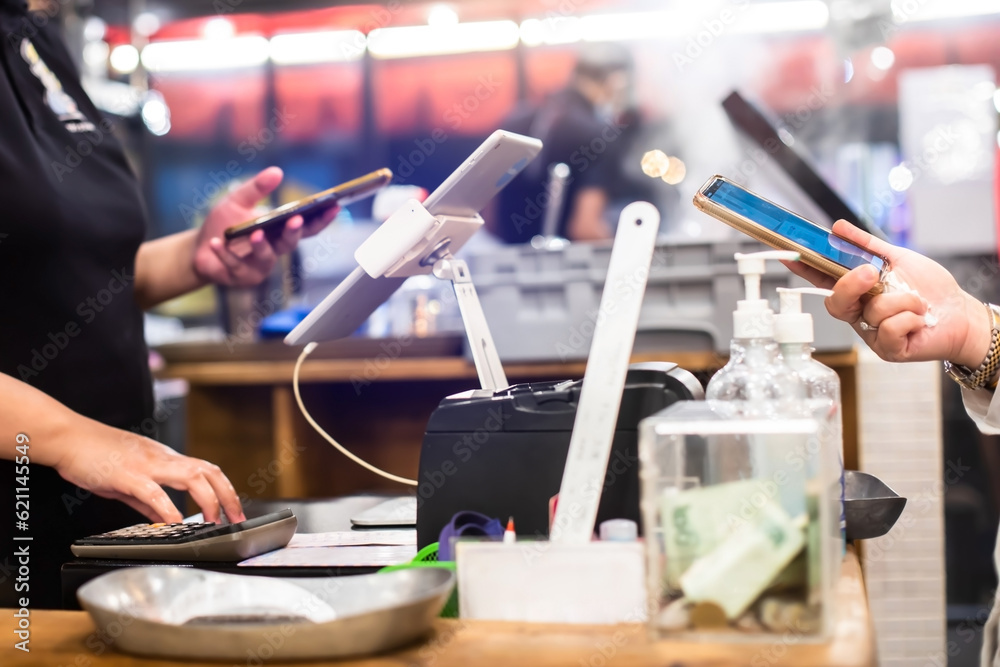 Fototapeta premium Selective focus to edge of smartphone in hand with blurry the tablet and cashier staff using it to receive orders from customers at counter service in cafe or store.