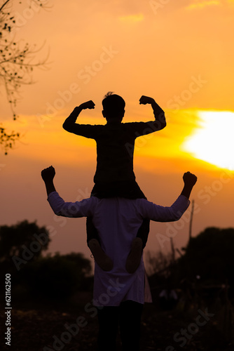 Father carrying son on shoulders on field against sky