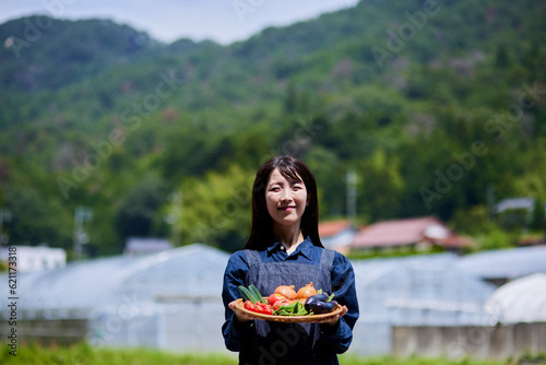 ビニールハウスの前で採れたての野菜をもつ農家の女性