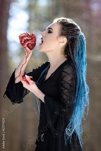 girl in black gothic dress with blue hair dreadlocks holding bloody heart