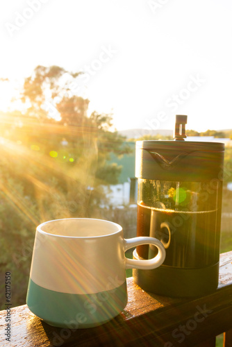 Vertical image of close up of coffee press and mug of fresh coffee at balcony on sunny day