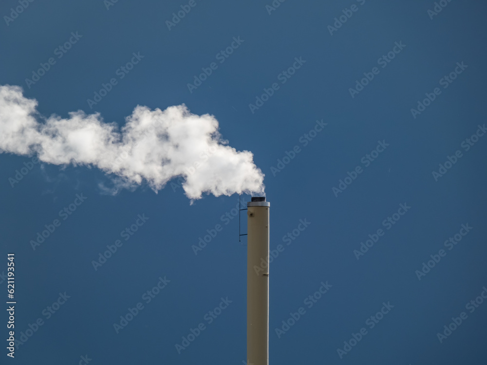 View of a huge metal chimney with white and grey dense smoke from burning firewood, pellets or briquettes View of a huge metal chimney with white and grey dense smoke from burning firewood, pellets or briquettes