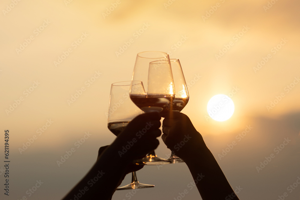 A group of girlfriends raise a glasses of white wine on the hill at picnic at amazing sunset.