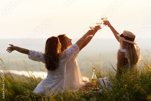 Obraz na płótnie Happy women in the park in evening sunlight. The lights of a sun. The company of female friends enjoys a summer picnic and raise glasses with wine. w salonie