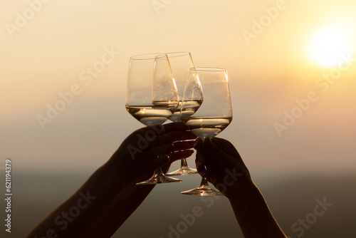 Close-up of hands holding glasses with white wine during sunset. Celebration and friendship concept.	
