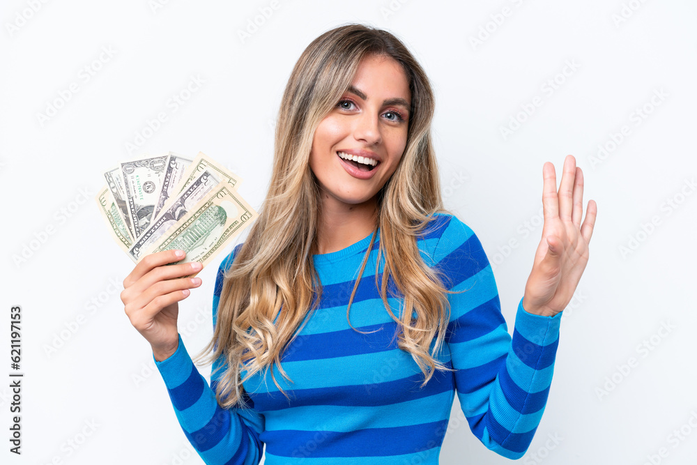 Young Uruguayan woman taking a lot of money isolated on white background saluting with hand with happy expression Young Uruguayan woman taking a lot of money isolated on white background saluting with hand with happy expression