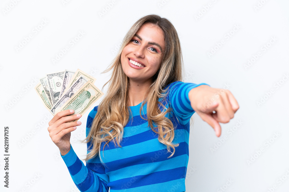 Young Uruguayan woman taking a lot of money isolated on white background pointing front with happy expression Young Uruguayan woman taking a lot of money isolated on white background pointing front with happy expression