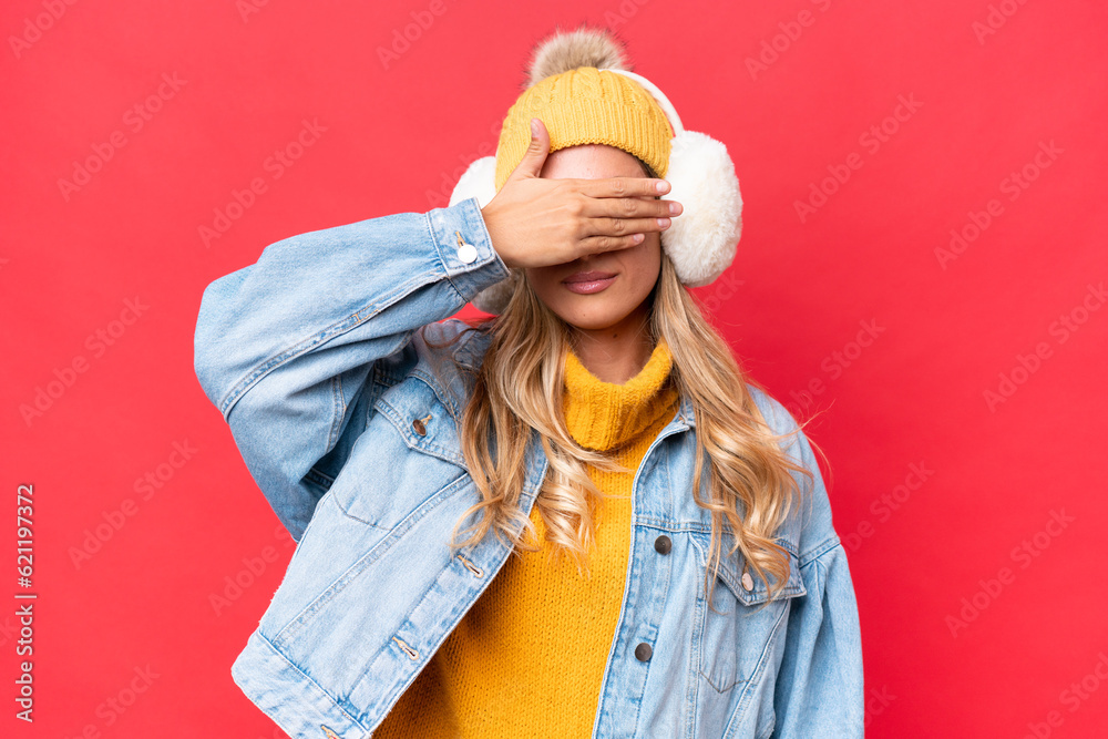 Young pretty Uruguayan woman wearing winter muffs isolated on red background background covering eyes by hands. Do not want to see something Young pretty Uruguayan woman wearing winter muffs isolated on red background background covering eyes by hands. Do not want to see something