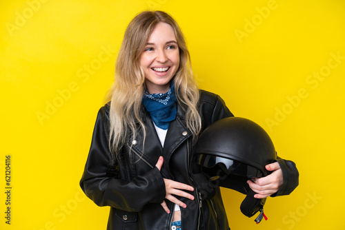 Blonde English young girl with a motorcycle helmet isolated on yellow background smiling a lot