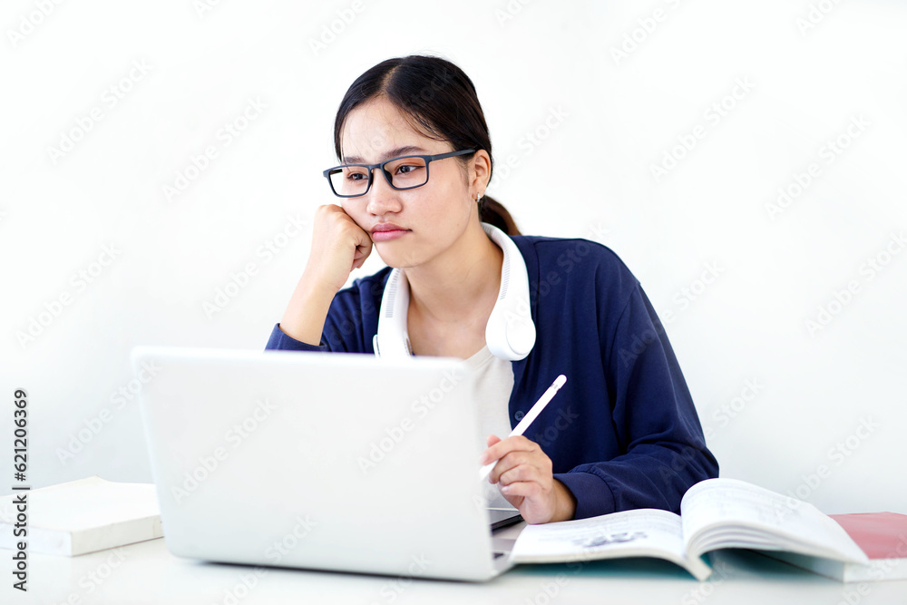 Closeup Asian young female student in casual cloth shows boredom in doing reports or homework with laptop on white gradient background. Asian school concept. Closeup Asian young female student in casual cloth shows boredom in doing reports or homework with laptop on white gradient background. Asian school concept.