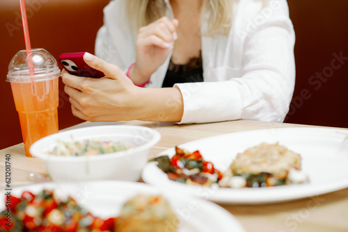 Lady sitting at cafe table with plates of food and holding smartphone in hand. Business lady working during lunch time.