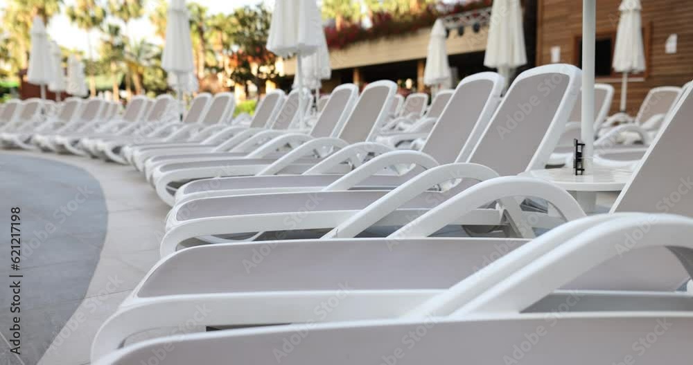 Row of stylish bright sun loungers and umbrellas by pool. Comfortable rest for tourists