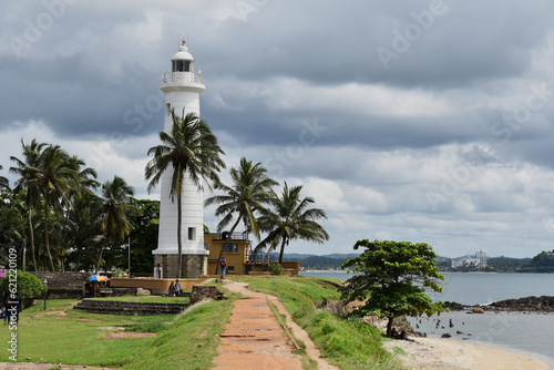 Galle Lighthouse before rain, Sri Lanka. Amazing white tower in Galle port. Pre-storm clouds usual for Ceylon landscape. Palm trees surround Galle Beacon creating unique exotic mood for visitors.