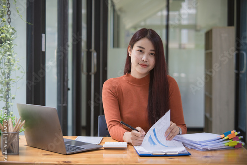 Free Download Thinking Asian businesswoman looking at financial statements and making marketing plans using a computer on her desk in the office holding report papers girl reading financial information. - GFXLoad