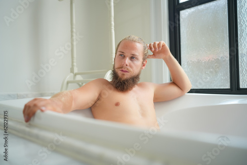 Relaxed young man bathing in modern bathroom luxury interior. Spa  wellness  body care concept