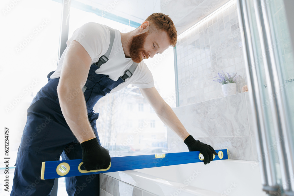 Man plumber installing white bath and control install. Repair service plumbing in bathroom Man plumber installing white bath and control install. Repair service plumbing in bathroom