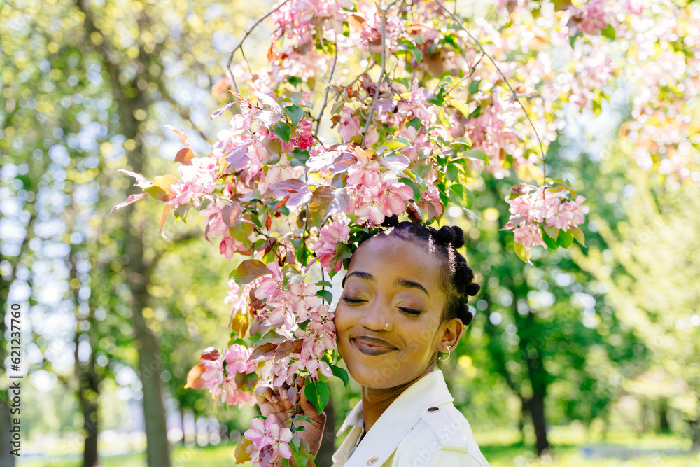 Obraz premium Black african american woman enjoy life and a beautiful park with sakura trees in bloom. Happiness, mental health concept.