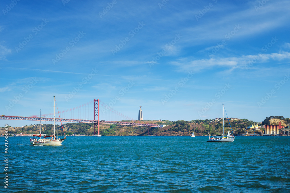 View of 25 de Abril Bridge famous tourist landmark over Tagus river, Christ the King monument and a tourist yacht boat. Lisbon, Portugal View of 25 de Abril Bridge famous tourist landmark over Tagus river, Christ the King monument and a tourist yacht boat. Lisbon, Portugal