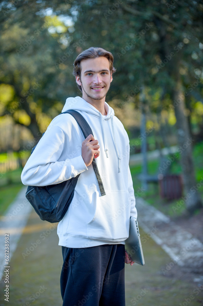 Portrait of a cheerful student with a laptop in his hands looking at the camera in the park. A student with a backpack and a computer in the park looks at the camera. Portrait of a cheerful student with a laptop in his hands looking at the camera in the park. A student with a backpack and a computer in the park looks at the camera.