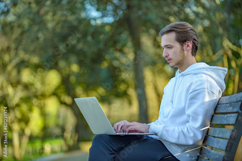 Young male freelancer works remotely at a computer on the Internet outdoors. Student is working at a laptop in the park. © Valua Vitaly