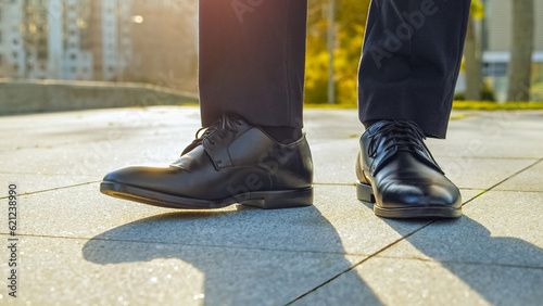Close-up view to the businessman in a black new classic  shoes outdoors. Legs of a businessman in fashionable glossy  shoes. Business concept. Stylish men wears. Low angle. Sun flares behind the legs
