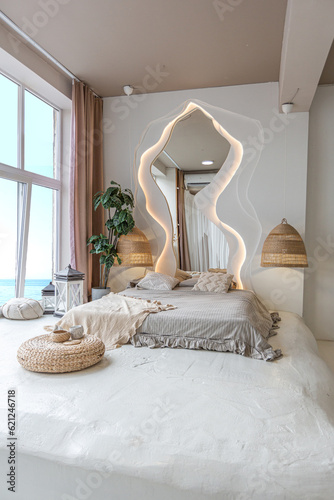 the interior of the bedroom in Balinese style by a large window with an awesome view of the sea. behind the bed is a curved mirror with LED illumination