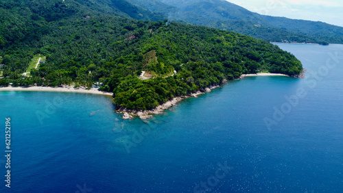 View of the sea and hills. Aerial view of a tropical island. Blue sea, sandy beach, jungle and white clouds over the horizon.