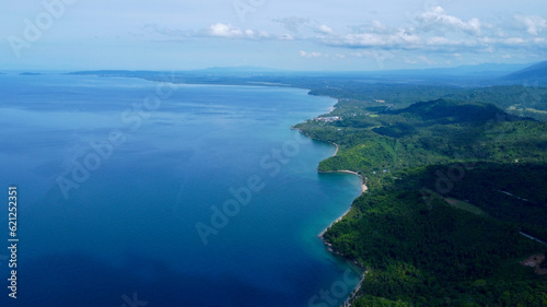 Aerial view of a tropical island. Blue sea, sandy beach, jungle and white clouds over the horizon.