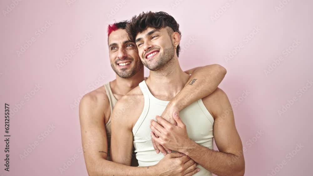 Two men couple smiling confident hugging each other over isolated pink background Two men couple smiling confident hugging each other over isolated pink background