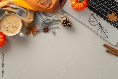 The comfort of remote job concept. Above view image of laptop with pumpkin decor, maple leaves, warm blanket and cup of hot chocolate on isolated grey background with empty space for text or advert