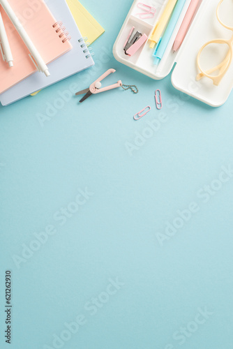 Embark on successful educational journey with top vertical photo of school supplies: notepads, pencil case and other items on a blue background. Use the empty circle to include text or advertisements