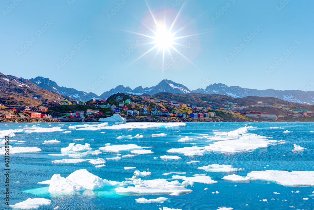 Fototapeta premium Melting of a iceberg and pouring water into the sea by the coast of Greenland - Picturesque village on coast of Greenland - Colorful houses in Tasiilaq, East Greenland