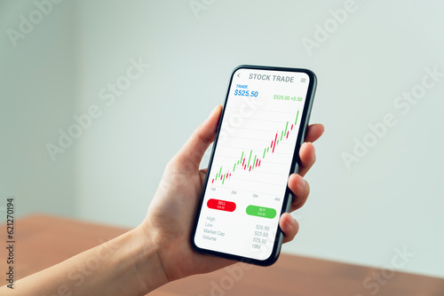 Businessman trader using smartphone with stock market investments and graph on screen to analyze trading data, buy or sell and checking price on mobile application.