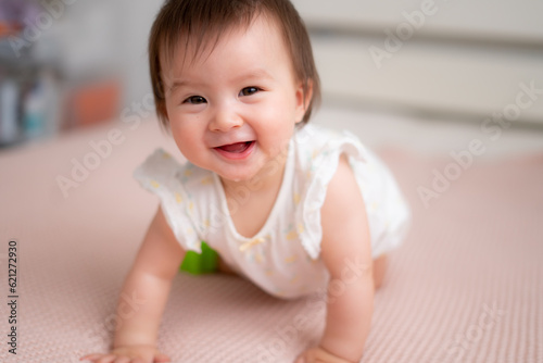 lifestyle home portrait of 9 months old mixed ethnicity Asian Caucasian baby girl playing happy and carefree on bed crawling and handling color blocks in childhood and nursery concept