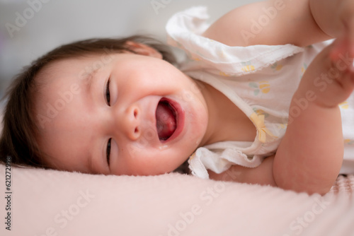 lifestyle home portrait of 9 months old mixed ethnicity Asian Caucasian baby girl playing happy and carefree on bed crawling laughing and excited in childhood and nursery concept
