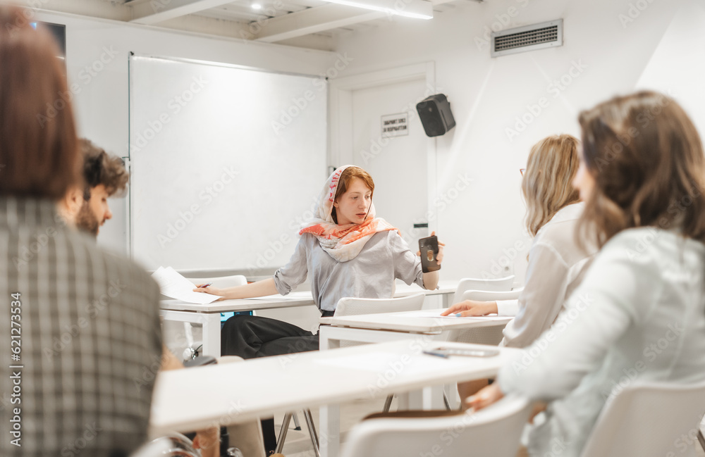 Fototapeta premium Ginger, muslim, female employee checking her phone while having a meeting at the classroom