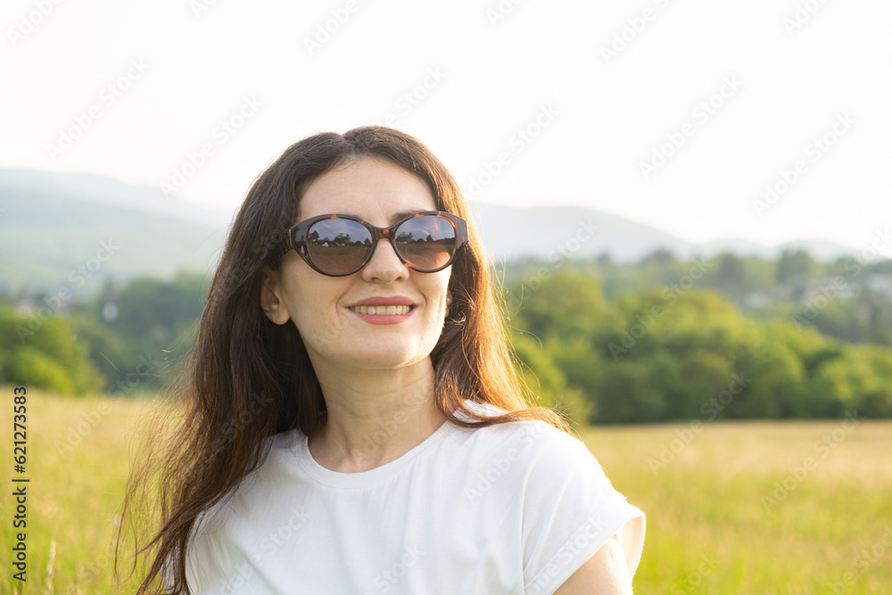 Portrait of a beautiful brunette woman wearing sunglasses at sunset in nature in summer Portrait of a beautiful brunette woman wearing sunglasses at sunset in nature in summer