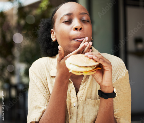 Hamburger, fast food and black woman eating a brunch in an outdoor restaurant as a lunch meal craving deal. Breakfast, sandwich and young female person or customer enjoying a tasty unhealthy snack photo