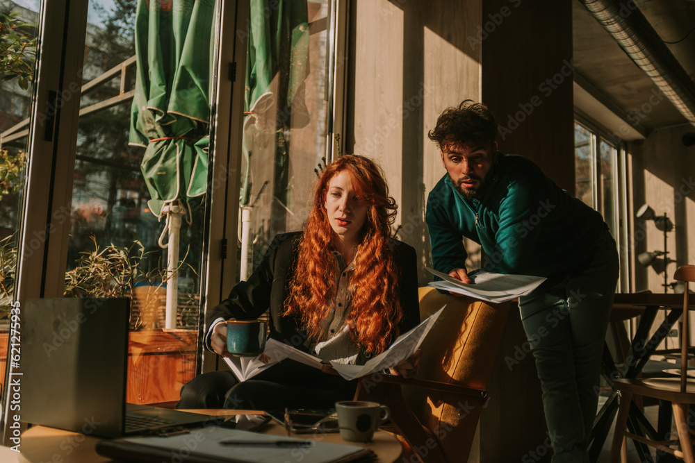 Lovely redhead woman is about to take a sip of her morning coffee while discussing business with her male colleague Lovely redhead woman is about to take a sip of her morning coffee while discussing business with her male colleague