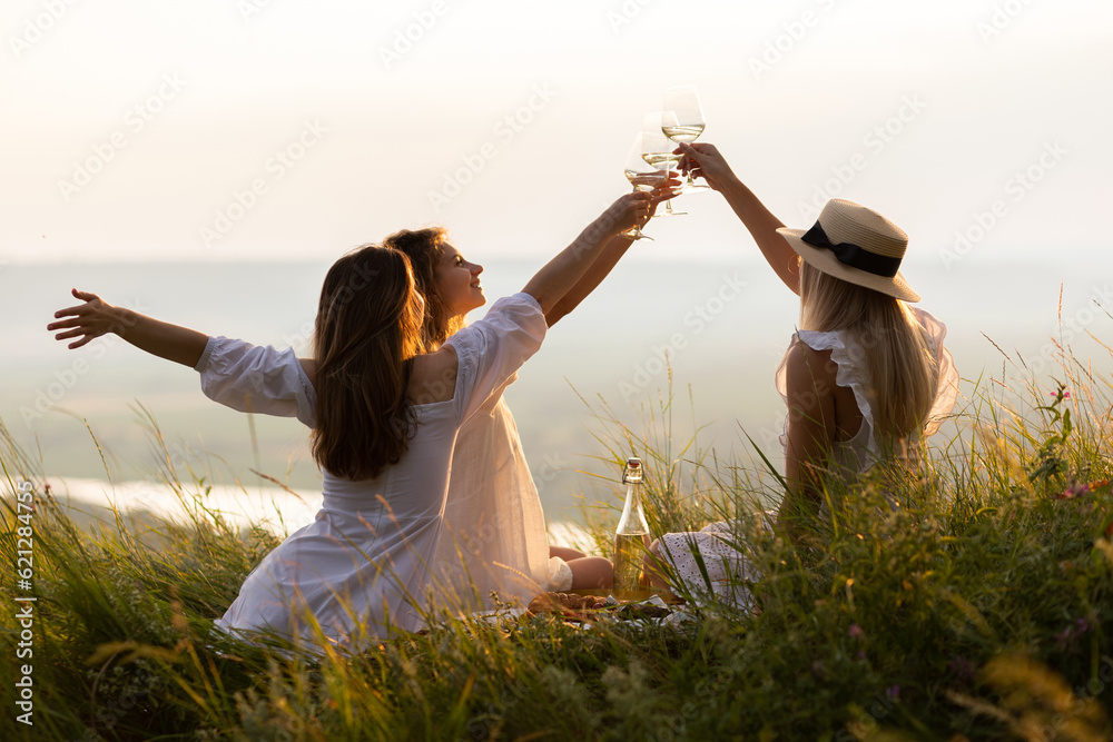 Summertime. Young happy girlfriends enjoyed picnic day on the hill at sunset. Lifestyle, vacation concept
