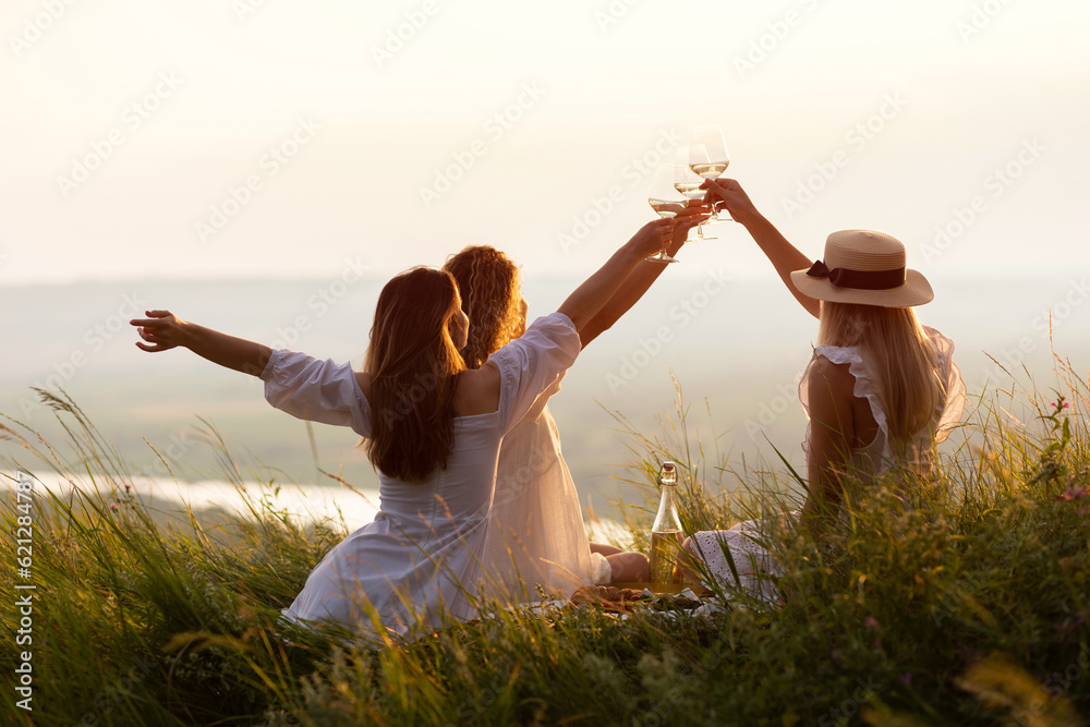 Best girlfriends enjoying hills view, drinking wine together. Happy people spending time picnic leisure together on the sunset.