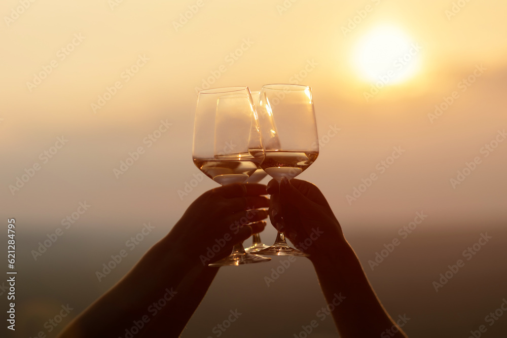 Three glasses of wine in hands of friends against the amazing sunset sky.