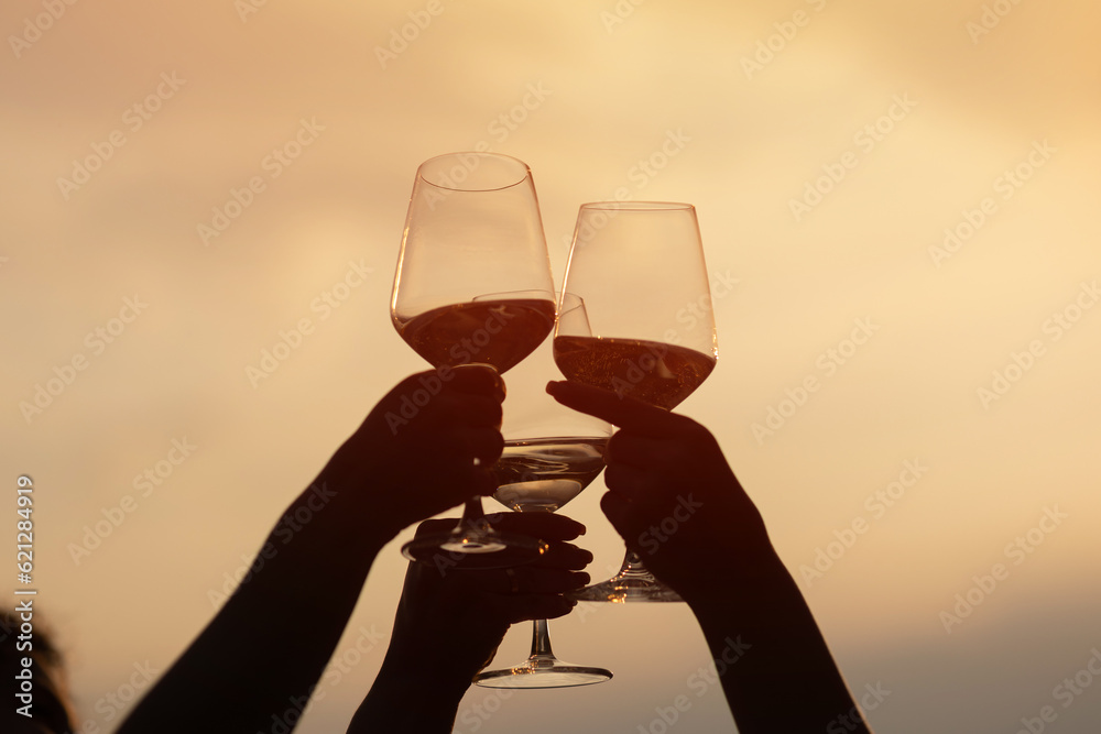 Friends clinking glasses with wine and enjoying wine against a beautiful sunset.