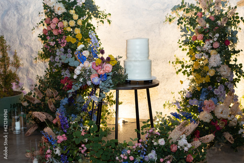 Obraz na płótnie White wedding cake in the evening. Cake on the background of an arch of fresh flowers. w salonie
