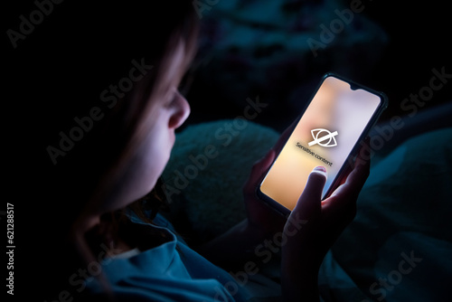 Fotografia A child using smart phone lying in bed late at night, playing games