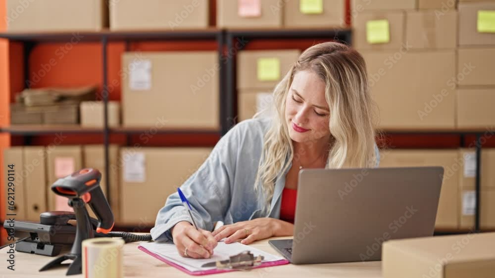 Young blonde woman ecommerce business worker using laptop writing on document at office Young blonde woman ecommerce business worker using laptop writing on document at office