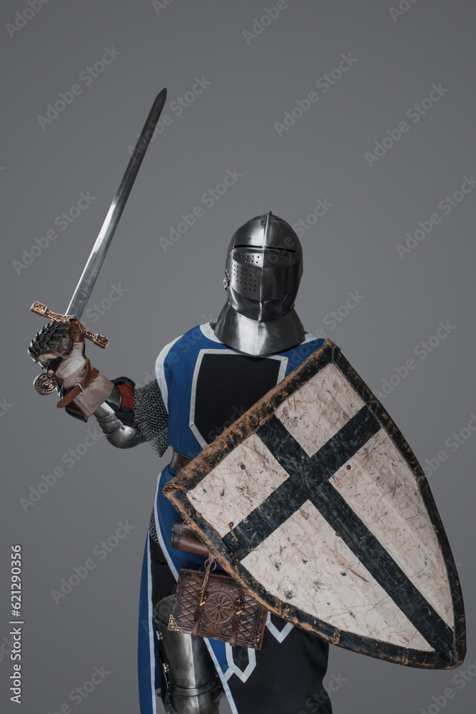 Naklejka premium Blue surcoat-wearing medieval knight actively swinging sword in battle on gray background