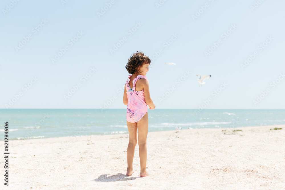 happy child girl wearing swimsuit feeding seagulls on beach day time. Lifestyle photography. Pastel colors happy child girl wearing swimsuit feeding seagulls on beach day time. Lifestyle photography. Pastel colors