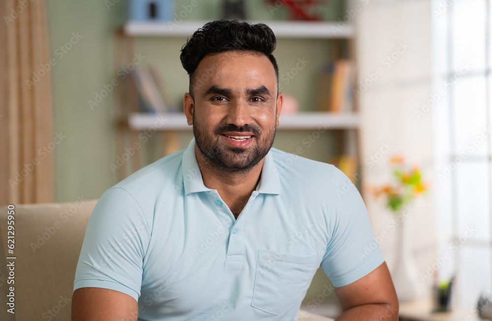 Happy smiling man looking at camera while sitting on sofa at home - concept of successful, satisfaction and relaxation Happy smiling man looking at camera while sitting on sofa at home - concept of successful, satisfaction and relaxation